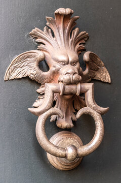 Decorative metal door knocker with winged lion head and ring on a historic doorway in Milan, Italy