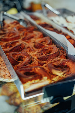 Close-up of glazed spiral cinnamon rolls arranged in a bakery display tray with serving tongs, warm golden-brown tones, and shallow depth of field