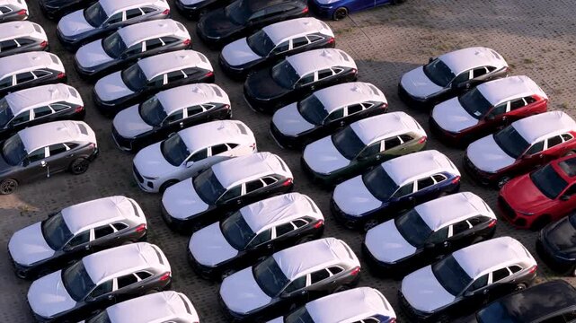 High-angle drone shot showing rows of parked brand-new cars at an industrial logistics and distribution facility, highlighting the automotive supply chain.