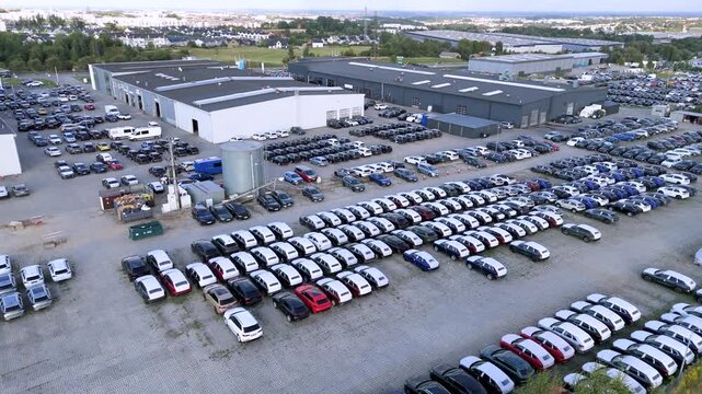 High-angle drone shot showing rows of brand-new vehicles parked at a distribution and logistics storage center, highlighting automotive supply chain operations and global trade.