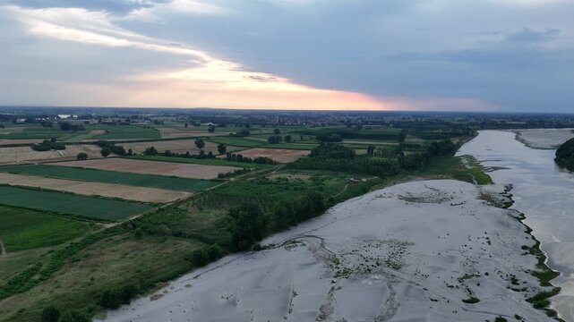 Po River drought exposes extensive pale sediment bars and shallow channels beside agricultural fields in the Po Valley of northern Italy, showing severe low water conditions, drone aerial shot.
