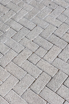 Close-up abstract texture of light gray rectangular stone paving blocks arranged in a staggered pattern. The rough natural surface and geometric layout create a minimalist architectural background