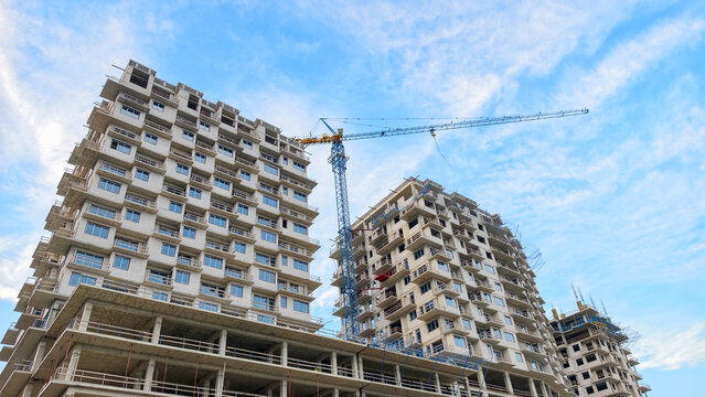 Multiple concrete high rise buildings under construction with a towering crane against a clear blue sky, showing urban development and the progress of modern architecture