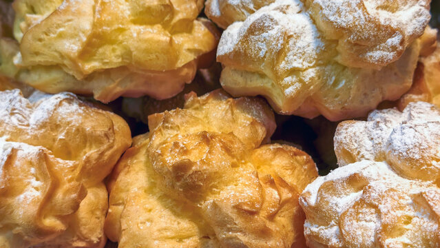 Golden choux pastry cream puffs generously dusted with powdered sugar, creating a visually appealing and delicious confectionery display for a bakery or patisserie