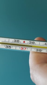 Close-up of a hand holding a thermometer showing a normal temperature reading