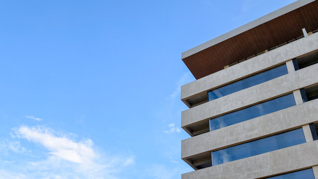 Modern building facade showcasing minimalist concrete architecture and large reflective windows against a clear blue sky, emphasizing urban development and contemporary design concepts
