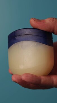 Close-up of a hand holding a petroleum jelly jar against a blue background