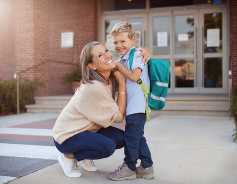 A mother hugging her son outside a school building. A happy mom embraces her boy with his backpack, depicting a back-to-school or reunion concept.