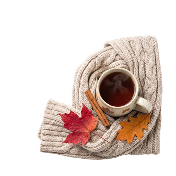 Mug of hot tea wrapped in knitted sweater with autumn leaves and cinnamon