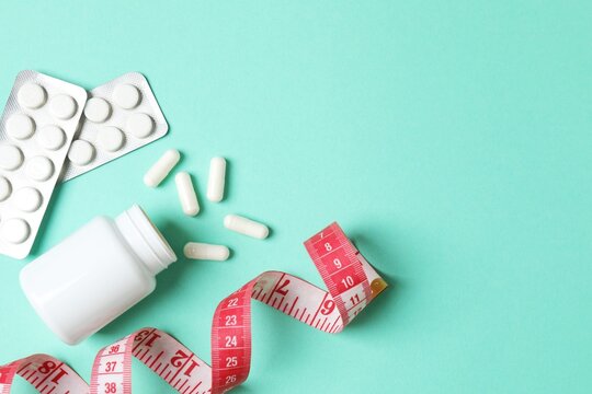 Jar of weight loss pills and measuring tape on color background, flat lay