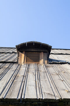 Low angle view of old wooden shingle roof dormer window against clear blue sky