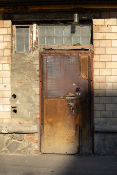 Weathered rusty iron door on old brick building wall with window transom