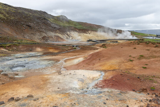Steaming hills and branching runoff spread through colorful terrain at Seltun on the Reykjanes Peninsula, Iceland. Red, yellow, grey and green mineral zones divide the valley beneath low cloud.