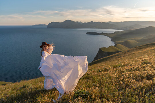 Woman dress mountain, a young woman in a white flowing dress poses on a cliff top overlooking a beautiful ocean landscape