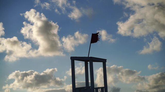 Red Flag Lifeguard Tower Clouds - A red flag on a lifeguard tower is raised indicating dangerous water conditions, with a background of clouds.