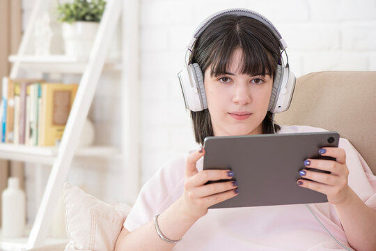 Young pretty brunette woman in headphones using tablet computer on modern living room interior background