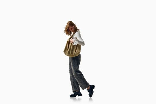 Fashionable woman walks with woven bag in white blouse and gray jeans. Concept of effortless style, casual fashion, accessories, movement and modern wardrobe.