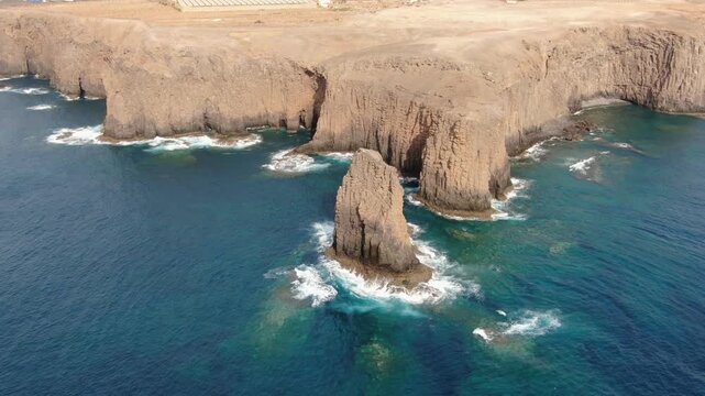 Rocky cliffs and a majestic sea stack known as Roque del Farallon on the Galdar coast of Gran Canaria, with turquoise ocean waves crashing