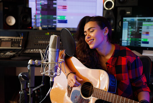 Woman with closed eyes singing in a recording studio and playing the acoustic guitar