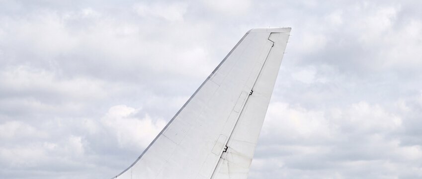 White airplane vertical stabilizer and rudder fin assembly stands out against soft overcast clouds during daytime airport ground stay