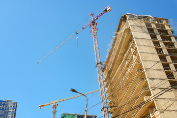 Bottom view tower crane works construction site high rise residential building scaffolding safety net clear blue sky background. © Elena