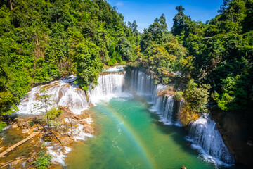 Fototapeta premium Aerial view of vibrant rainbow over turquoise river pool with waterfall cascading in lush green forest at Glue-Thor Waterfall (Kyone Htaw Waterfall), Kayin State, Myanmar.