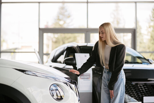 Young woman choosing new car in dealership showroom