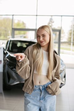 Young woman pointing new car in dealership showroom