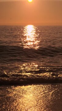 Golden sunset ocean waves wash over a sandy beach under a glowing horizon. Static wide shot.