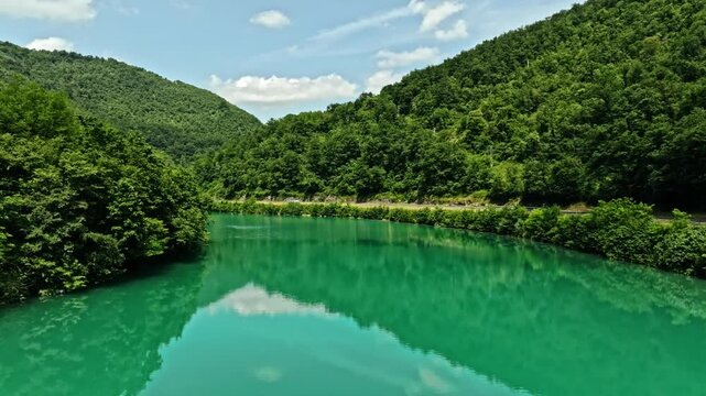 Cinematic drone shot flying forward above the emerald green Soca river valley. Empty country road tracking on the right side under a soft sky with beautiful rolling alpine hills at the horizon.
