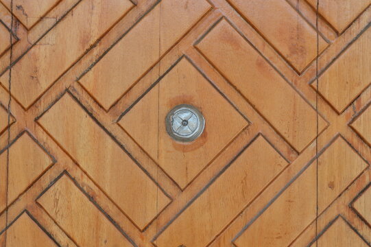 Close up of a carved wooden panel with a geometric diamond pattern and a central rustic metal stud. Rich natural brown wood grain texture, ideal for architectural backgrounds and vintage designs.