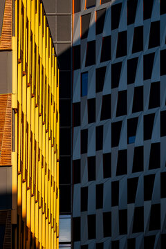 Yellow sunlit facade beside a dark modern building creates a bold vertical contrast of windows and geometric patterns in an urban architectural detail