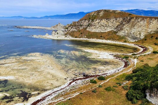 Kaikoura, New Zealand - Rugged Coastal Cliffs With Light Rock Formations, Curving Shoreline Path, Blue Sea And Mountain Backdrop, Partly Cloudy Sky, Travel Photography Suitable For Tourism Marketing.
