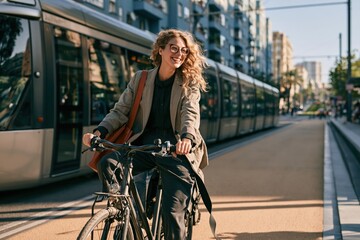 Plakat Young businesswoman riding a commuter bicycle on a dusty city street, smiling with a burnt orange bag for sustainable urban transport and eco-friendly travel