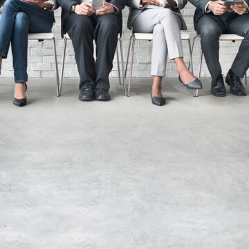 Four people seated, legs visible, in business attire against a brick wall.