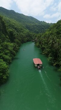 Vertical drone follows Loboc River cruise boats as they pass each other on green water between forested hills in Bohol