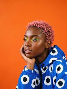 Stylish Black woman with pink hair and neon makeup, vibrant Gen Z fashion portrait on orange background, trendy blue patterned hoodie