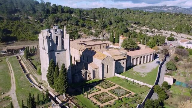 Lagrasse Abbey (Abbaye Sainte-Marie de Lagrasse). Panoramic aerial view of the cloisters, tower, gardens, and monastery vegetable plots next to a wooded hill. Benedictine monastery. Aude. France.