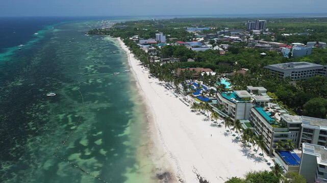 Slow aerial flyover along Alona Beach, showing white sand, shallow turquoise water, boats, resorts, and the Panglao coastline in Bohol