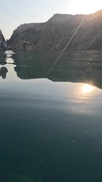 Sea, Mountains, Reflection, calm water reflects rocky cliffs at sunset. Vertical video.