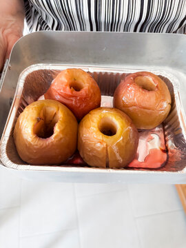 Person serving a foil tray of four cored, roasted apples, golden and tender, ready as a warm homemade autumn dessert or healthy snack in a rustic kitchen setting