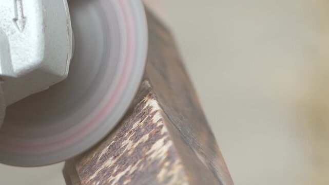 Rotary grinder disk removes corrosion from a heavy iron beam inside a fabrication shop. Close-up high angle shot.