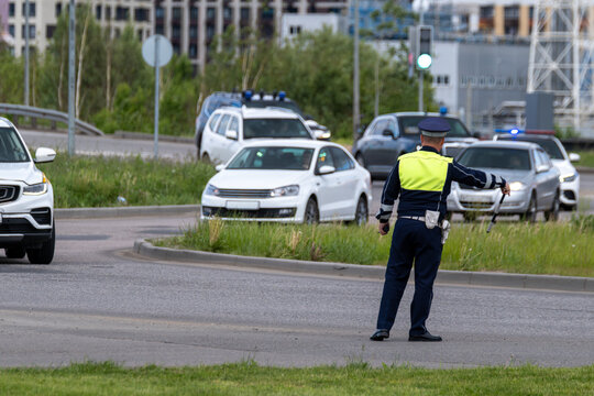 Uniformed police officer directs traffic at busy urban intersection, managing stopped cars and patrol vehicles during daytime.