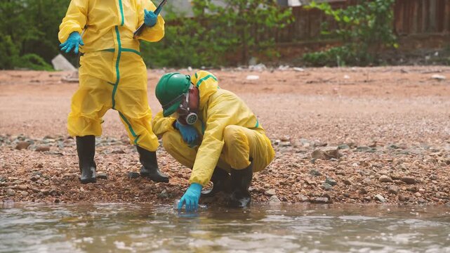 Environmental technicians examining soil and water contamination near polluted area, wastewater inspection, pollution assessment, environmental sampling, field research.