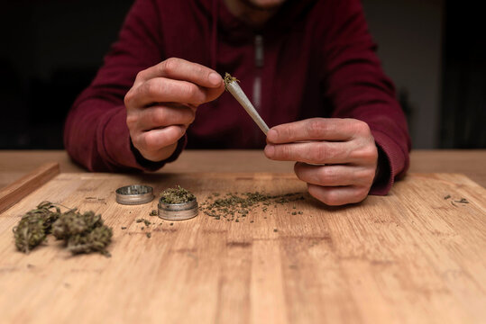 Close up of Man filling joint with legal cannabis and a grinder on a wooden board