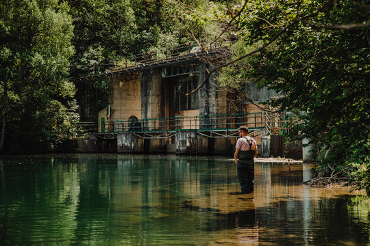 Man fly fishing in a river near an old dam in the forest