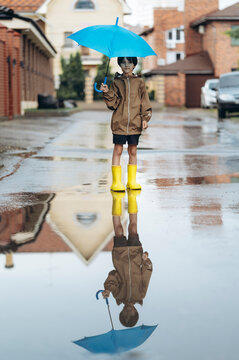 A boy in a raincoat holds an umbrella over a puddle