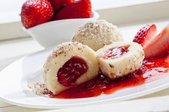 Curd cheese dumpling with strawberry filling and grounded hazelnut on plate, close up