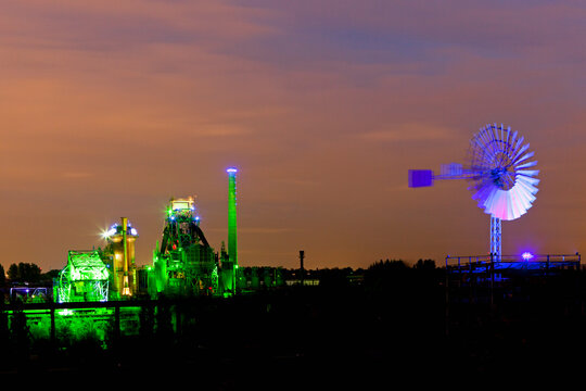 Germany, Nordrhein-Westfalen, Duisburg, Duisburg-Nord Landscape Park, View of illuminated blast furnace and wind mill of industrial plant at night