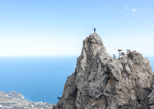 Man standing on mountain peak with arms outstretched over the sea